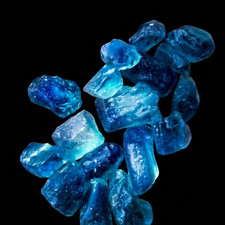 A parcel of rough aquamarine crystals on a black background, ranging from pale sky blue to deep saturated blue