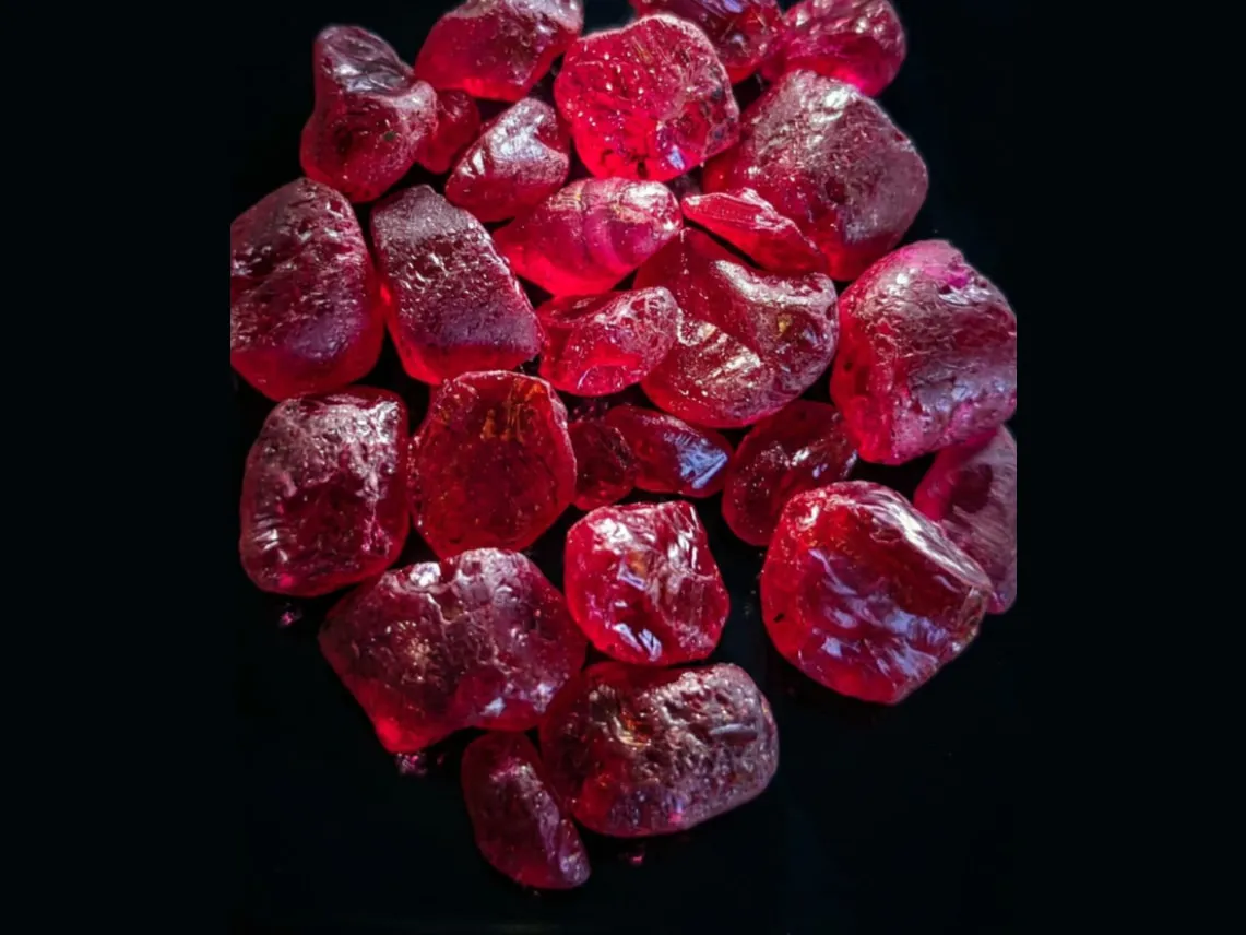 A parcel of rough ruby crystals on a black background, showing deep red saturation and natural crystal surfaces
